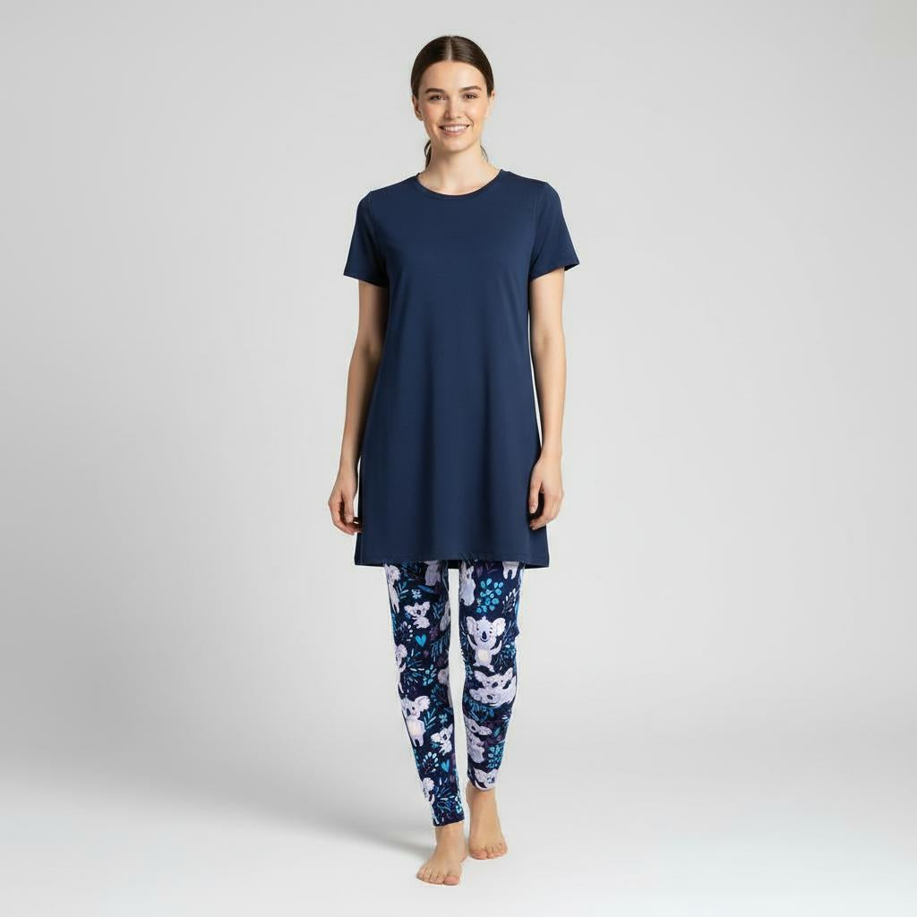 Woman wearing a navy blue tunic and koala patterned leggings on a light grey background
