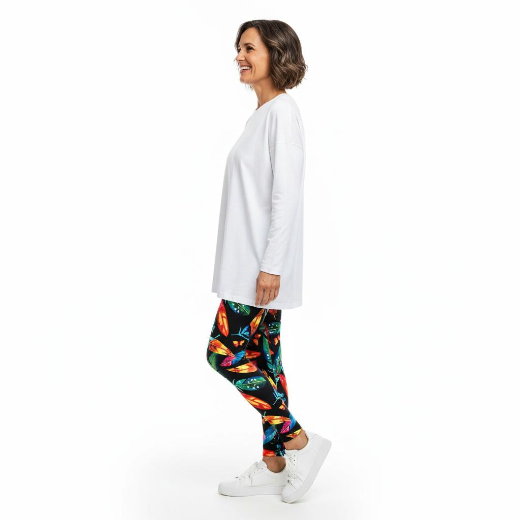 Woman wearing a white long-sleeve top and colourful feather leggings on a white background