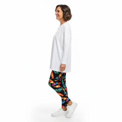 Woman wearing a white long-sleeve top and colourful feather leggings on a white background