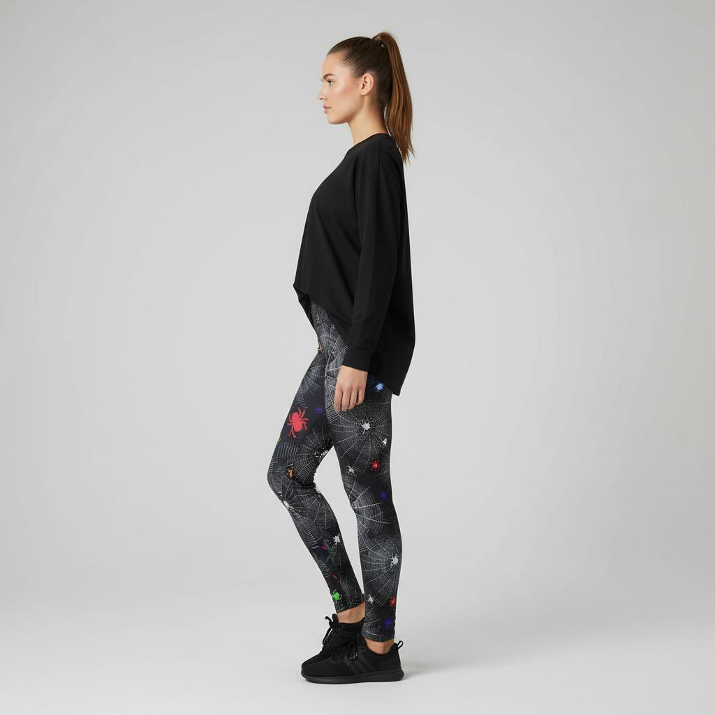Woman wearing black long-sleeve top and spider and web patterned leggings on a grey background
