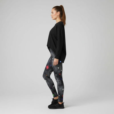 Woman wearing black long-sleeve top and spider and web patterned leggings on a grey background