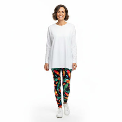 Woman wearing a white long-sleeve top and colourful feather patterned leggings on a white background