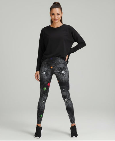 Woman wearing black long-sleeve top and spider and web patterned leggings on a grey background